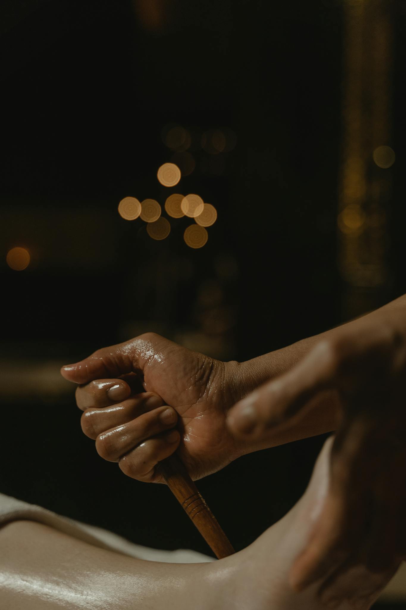 A detailed view of a hand using a wooden stick during a foot massage treatment.